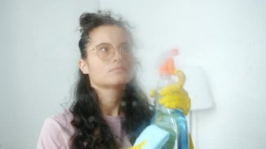 Kadın temizlikçinin portresi kameraya dönüyor. Suyu püskürtüyor ve evde yıkıyor.