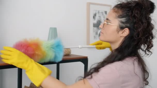Молодая азиатка в резиновых перчатках вытирает мебель дома, заботясь о гигиене — стоковое видео