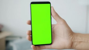Kapalı alandaki yeşil krom ekran akıllı telefonu tutan erkek elinin yakın çekimi.