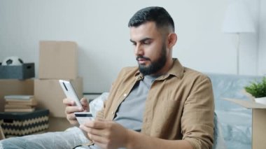 Orta Doğulu adam yeni evde akıllı telefon kullanarak kredi kartıyla ödeme yapıyor.