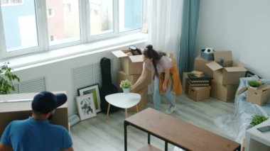 Yeni eve karton kutular getiren ve kadın ev sahibiyle konuşan genç bir erkek çalışanın yüksek açılı görüntüsü.