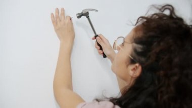 Evde tek başına çalışan kadın elleri duvara çivi çakıyor.