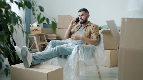 Ny husägare talar på mobiltelefon sittande i lägenhet med packade tillhörigheter — Stockvideo