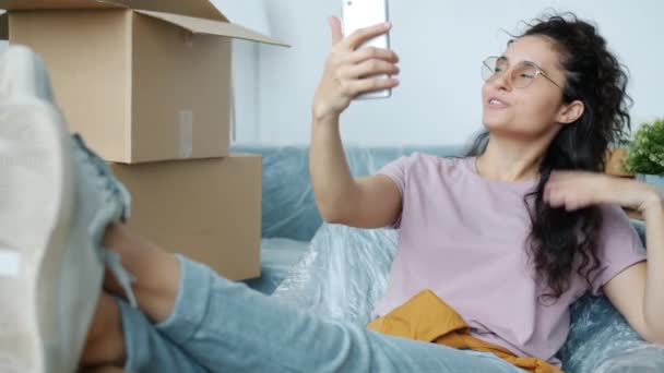 Vrolijke jonge vrouw chatten op video bellen in nieuw huis na verhuizing wijzend naar dozen — Stockvideo