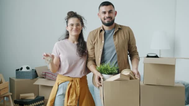 Retrato de feliz jovem casal sorrindo olhando para câmera segurando a chave da casa e caixas durante a realocação — Vídeo de Stock