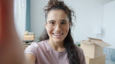 Taşınırken yeni daireden online video görüşmesi yapan neşeli genç bir kadının portresi.