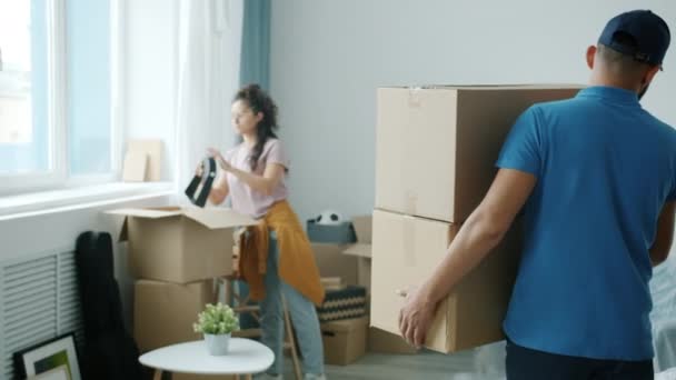 Mannelijke verhuizer draagt uniform brengen kartonnen dozen naar vrouwen nieuw appartement — Stockvideo