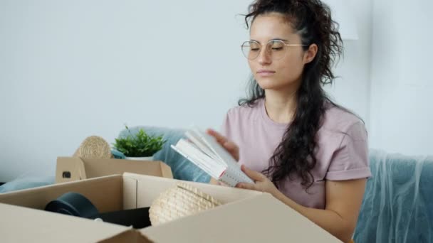 Slow motion portrait of attractive mixed race girl going through personal stuff unpacking box after relocation — Stock Video