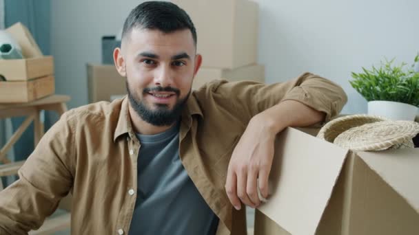 Портрет хлопця з Близького Сходу, який сидить у новому будинку з коробками. — стокове відео