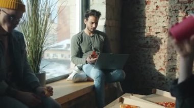 Ofiste pizza yiyen çeşitli iş adamları gündüzleri dizüstü bilgisayarla konuşur ve konuşur.