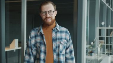 Ofiste tek başına kameraya bakarak duran genç iş adamının yavaş çekim portresi.