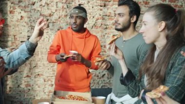 Neşeli erkekler ve kadınlar modern ortak ofiste pizza ve kaygısız sohbetin tadını çıkarıyorlar.