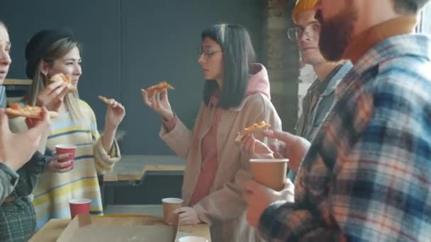 Grupo multirracial de jóvenes hablando y comiendo pizza en el lugar de trabajo durante la pausa para el almuerzo — Vídeos de Stock