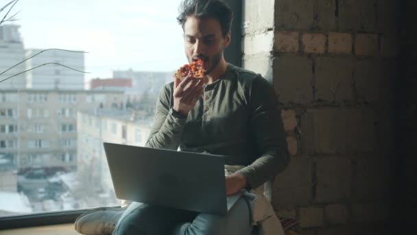 Арабский бизнесмен ест пиццу и работает с ноутбуком в помещении в мансарде — стоковое видео