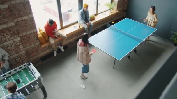 Щасливі молоді люди розслабляються під час робочої перерви граючи в пінг-понг і фосбол в офісі — стокове відео