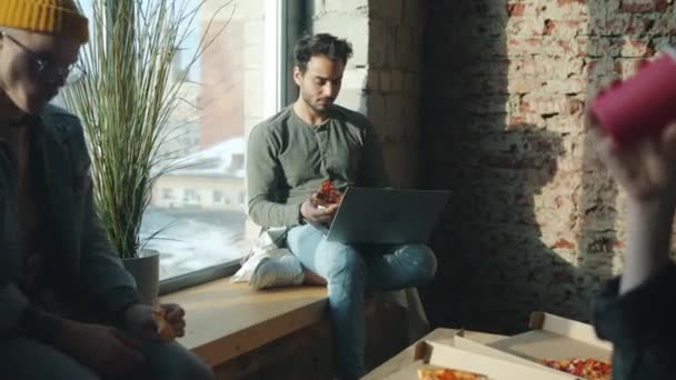 Różnorodna grupa biznesmenów jedzących pizzę w biurze rozmawiających i korzystających z laptopa w ciągu dnia — Wideo stockowe