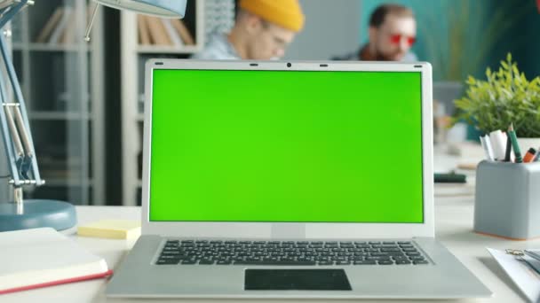 Chroma pantalla verde de la llave portátil en el escritorio con los empleados que se mueven en segundo plano en la oficina — Vídeos de Stock