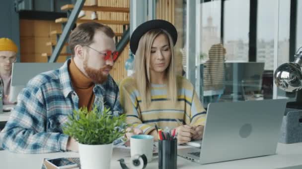 Beyaz erkek ve Asyalı kadın meslektaşlar ofiste dizüstü bilgisayar kullanarak konuşuyorlar. — Stok video