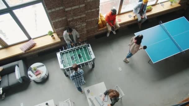 Вид зверху на колег, які грають у фосбол і пінг-понг в приміщенні в сучасному коворкінгу — стокове відео