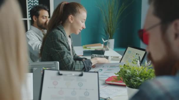 Groep van ondernemers die werken met documenten die grafieken bestuderen die aan een bureau in een gedeeld kantoor zitten — Stockvideo