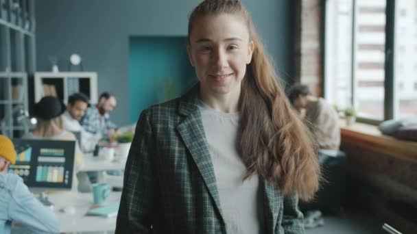 Mooie zakenvrouw staat binnen in modern gedeeld kantoor glimlachend kijkend naar de camera — Stockvideo