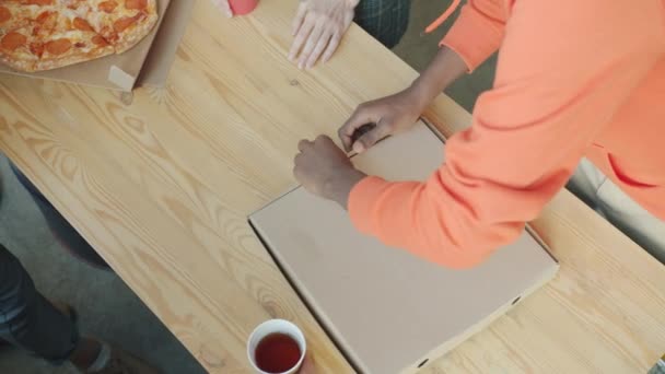 Close-up de mãos masculinas trazendo pizza e caixa de papelão de abertura na mesa de madeira no escritório — Vídeo de Stock