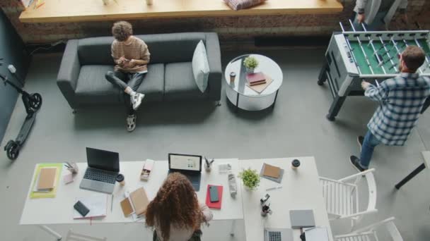Blick von oben auf junge Mitarbeiter, die entspannt im Großraumbüro arbeiten und spielen — Stockvideo