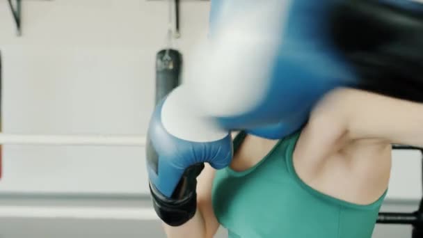 Joven luchador con guantes y casco protector perforando y mirando a la cámara en el gimnasio — Vídeos de Stock