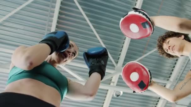 Χαμηλή γωνία βολή της νεαρής γυναίκας εξάσκηση κινήσεις πυγμαχίας με γυναίκα εκπαιδευτή σε εσωτερικούς χώρους γυμναστήριο — Αρχείο Βίντεο