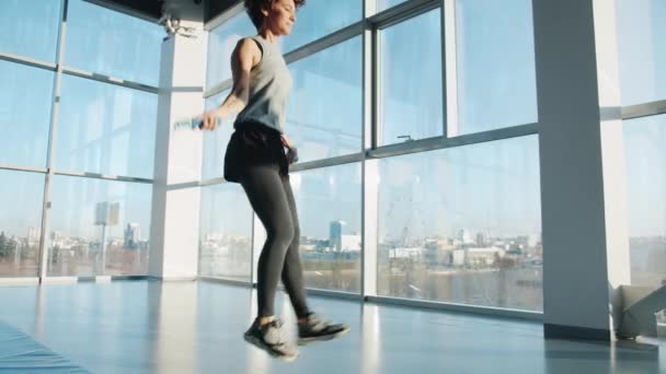 Młoda kobieta w odzieży sportowej skacze ze skakanką w domu w nowoczesnej siłowni — Wideo stockowe