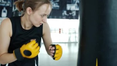 Kickboksçu motive olmuş eldiven giyiyor, spor salonunda kum torbası kullanıyor.