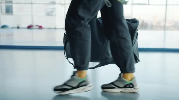 Spor çantasıyla modern spor salonunda yürüyen genç bir kadının yan görüntüsü. — Stok video