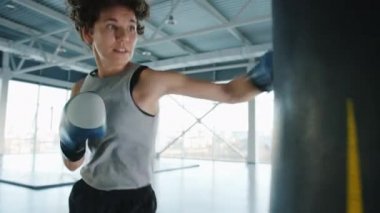 Güçlü genç bir kadın boks salonunda tek başına kum torbası eğitimini yeniyor.