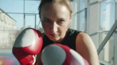 Spor salonunda dövüşen ve kameraya bakan eldivenli genç bayan boksörün portresi.