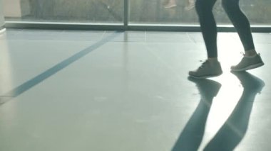 Spor salonunda panoramik pencereye karşı boks yapan genç bir kadının arka ışıklandırılmış silueti.