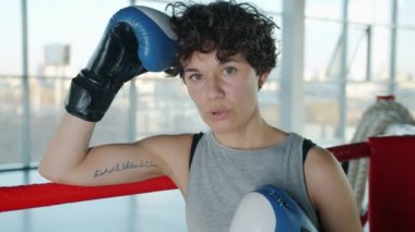 Ağır çekimde yorgun ve terli kadın boksör ringin köşesinde rahat rahat nefes alıyor.