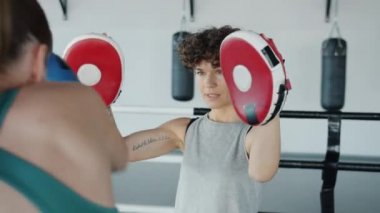 Kadın boks antrenörünün spor salonunda birlikte antrenman yapan sporcu kadını yavaş çekimde izlemesi.
