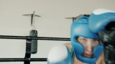 Koruyucu kask ve eldiven takan kendine güvenen boksör kız spor salonunda kameraya bakıyor.