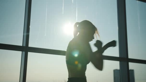 Silueta iluminată din spate a unei tinere femei care aruncă pumni lucrând în sala de sport modernă — Videoclip de stoc