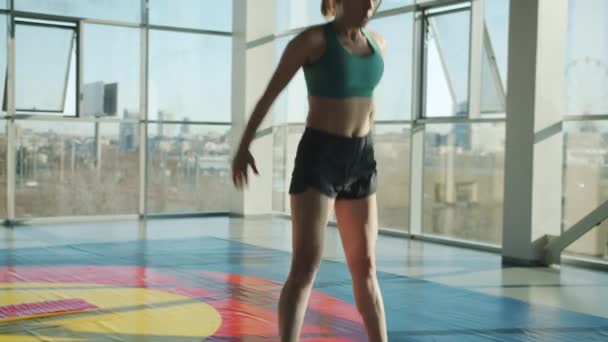 Hermosa mujer joven haciendo ejercicio en la pared de cristal moderno gimnasio saltando entrenamiento solo — Vídeos de Stock