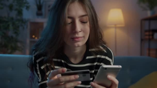Mujer joven emocionada pagando con tarjeta de crédito utilizando teléfono inteligente en el interior de casa por la noche — Vídeos de Stock