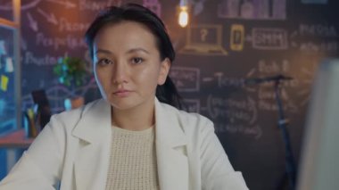 Çekici esmer iş yerindeki karanlık yaratıcı ofiste kameraya bakıyor.