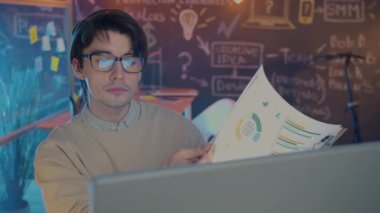 Bilgisayarla çalışan ve karanlık ofiste doküman okuyan çekici genç adam portresi.