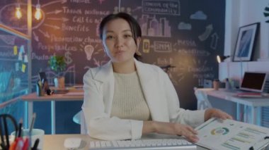 Hırslı Asyalı iş kadını internette video görüşmesinde sunum yapıyor geceleri masa başında oturuyor.