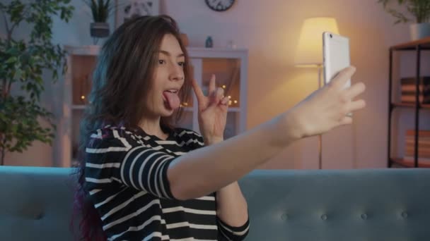 Flot ung dame tager selfie ved hjælp af smartphone kamera i belyst lejlighed – Stock-video