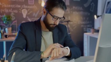 Geç saatlere kadar çalışan akıllı saati kullanan ciddi bir iş adamının ağır çekimde portresi.