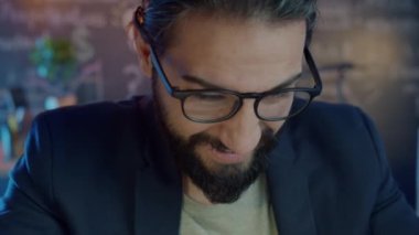 Mobil video oyunu oynayan iş adamının yakın plan görüntüleri akıllı telefon ekranına dokunuyor ve karanlık ofiste gülümsüyor.