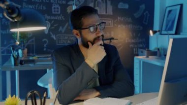 Düşünceli bir çalışanın portresi bilgisayar ekranına bakıp sonra parmağını kaldırarak gece fikir üretmek.