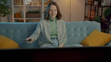 Neşeli genç bayan gülerek evde televizyon izleyerek eğleniyor.