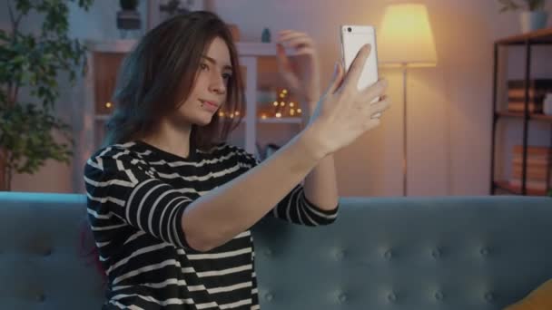 Akşamları evde akıllı telefon kamerasıyla selfie çeken çekici genç bir kadın. — Stok video